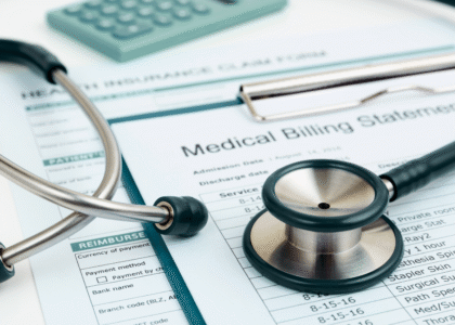 Close-up of a stethoscope, calculator, and health insurance claim form placed on top of a medical billing statement.