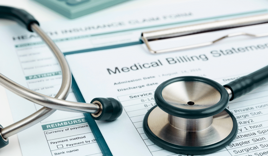 Close-up of a stethoscope, calculator, and health insurance claim form placed on top of a medical billing statement.
