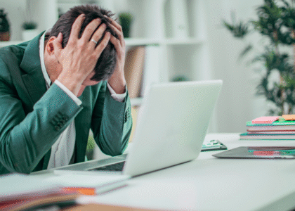 Stressed man holding head at desk with laptop.