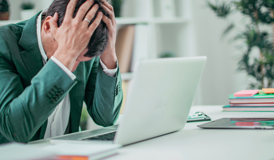 Stressed man holding head at desk with laptop.